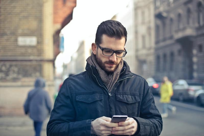 hombre con gafas y abrigo enviando mensajes de texto por el móvil