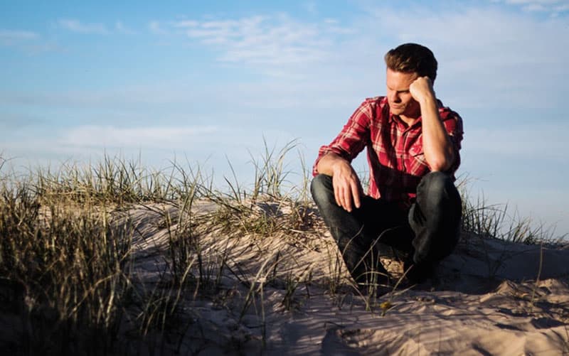 man in polo thinking while sitting on the ground with few grass