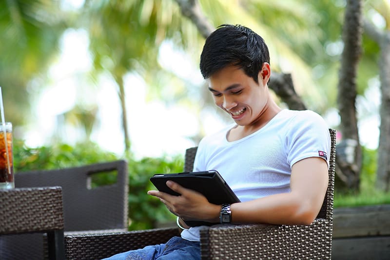 uomo in camicia bianca che utilizza il computer tablet mentre è seduto all'aperto
