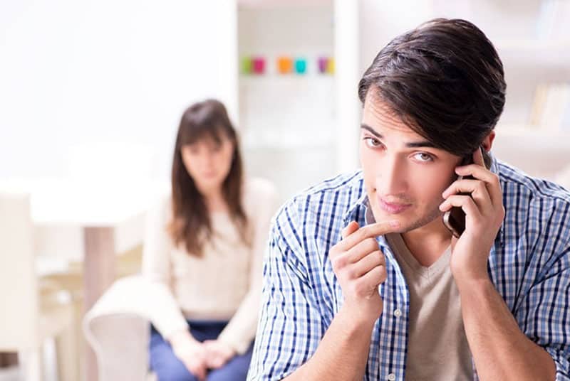 un hombre atiende el teléfono a distancia de una mujer sentada en un sofá