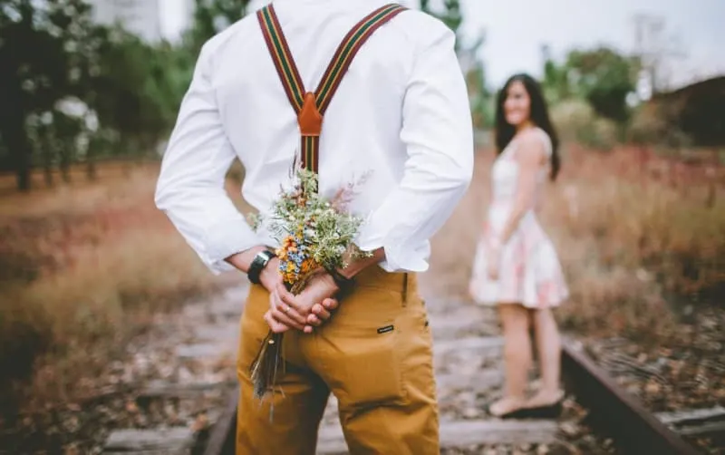 man keeping flowers at his back while looking at a woman