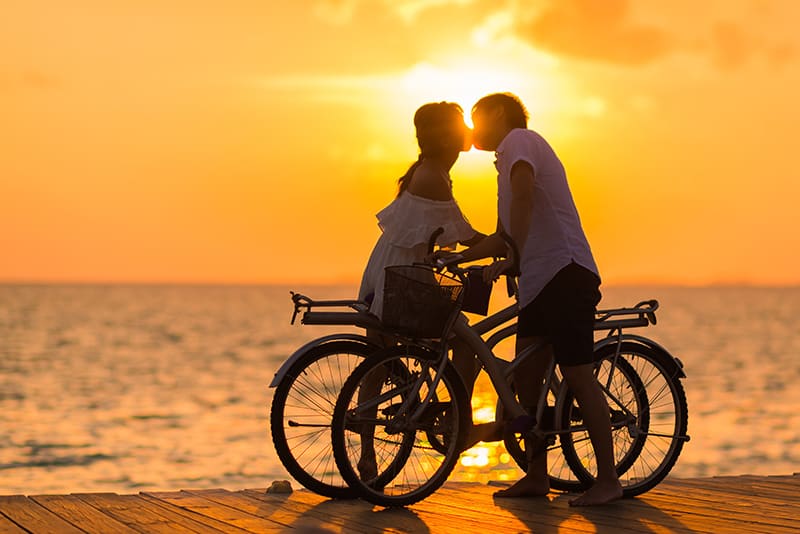 man kissing a woman while holding bicycle during the sunset