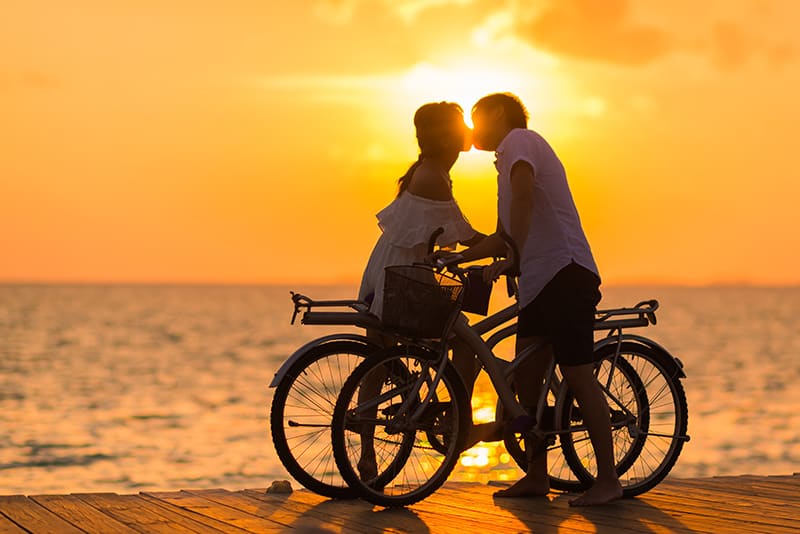 homem a beijar uma mulher enquanto segura uma bicicleta durante o pôr do sol