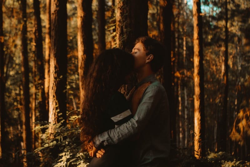 man kissing woman on forehead in forest