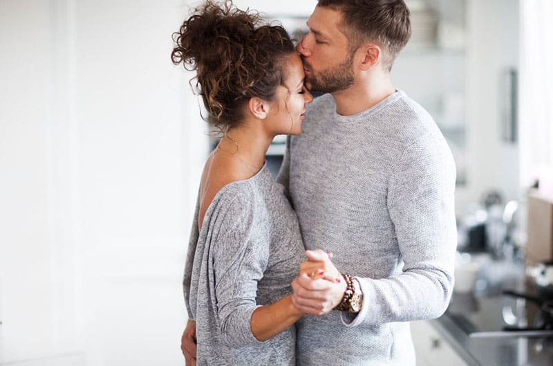 man kissing forehead of a woman both are wearing gray top