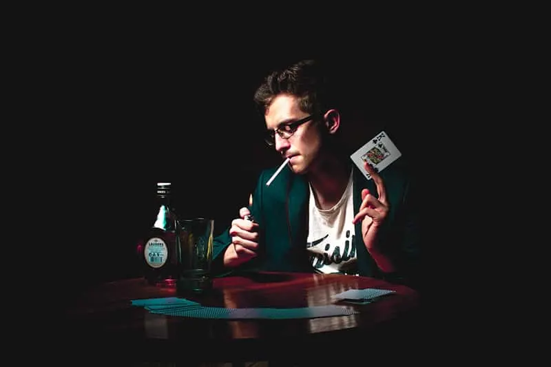 man lightening the cigarette and holding playing card in his hand