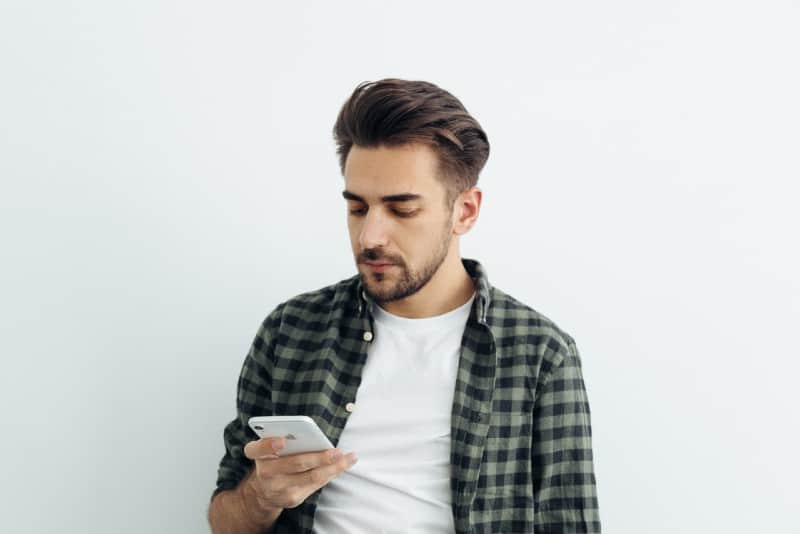 man in checked shirt using phone near white wall