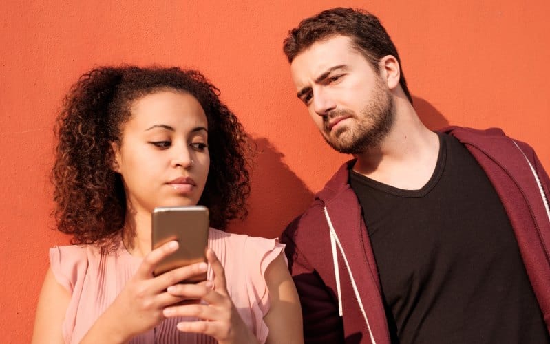 Hombre de pie junto a una mujer y mirando el teléfono móvil que ella sostiene en sus manos