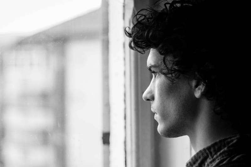 hombre con el pelo rizado mirando por la ventana