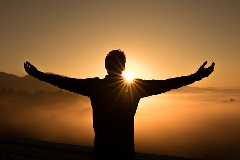 uomo su una scogliera che alza le mani durante il tramonto