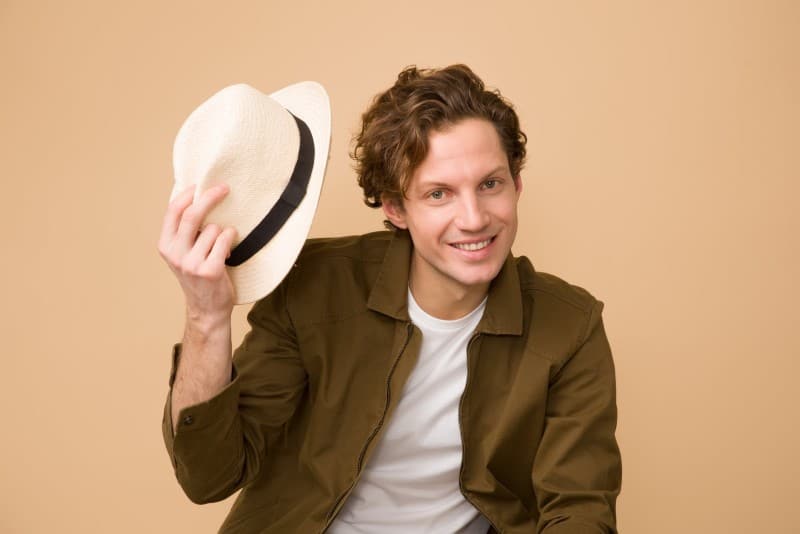 man in khaki jacket holding hat and sitting indoor