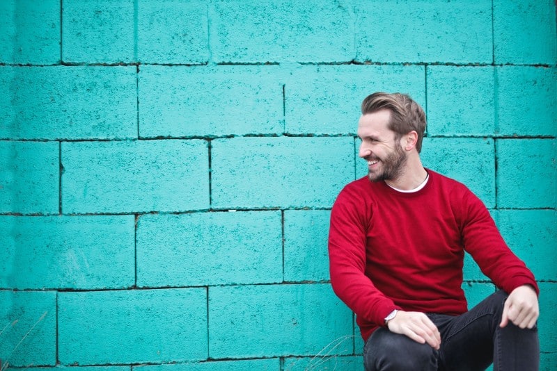 man in red sweater sitting near blue wall