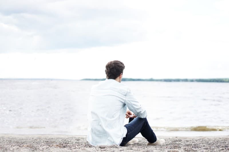 man with white shirt sitting near water