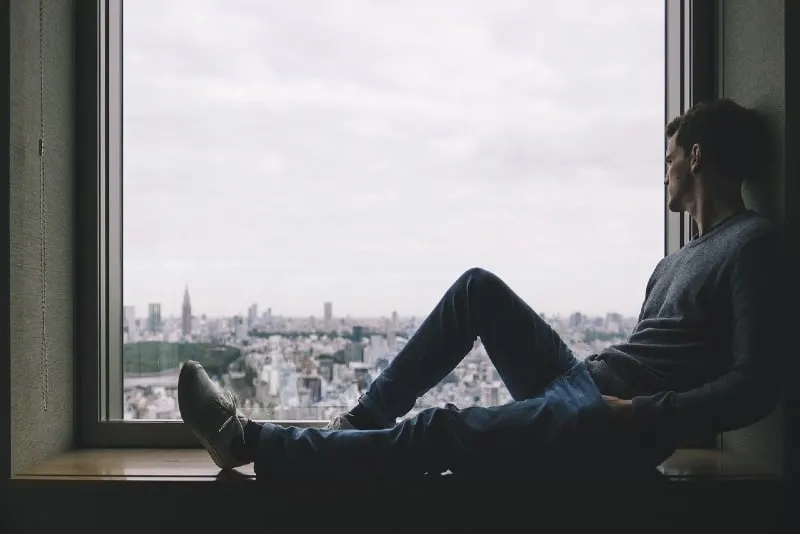 man sitting near window while looking at city