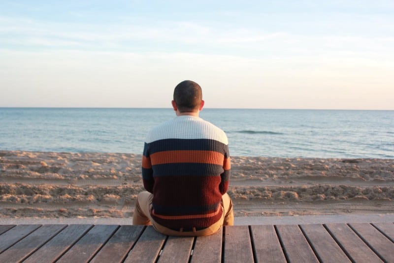 uomo seduto su un pannello di legno che guarda l'oceano