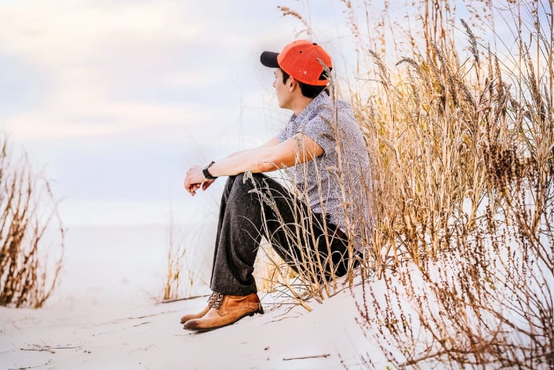 man sitting on sand with wheat looking right during daytime