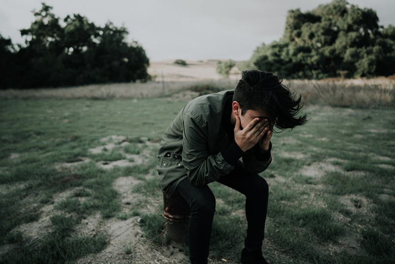 man sitting on stool chair while covering his face with hands