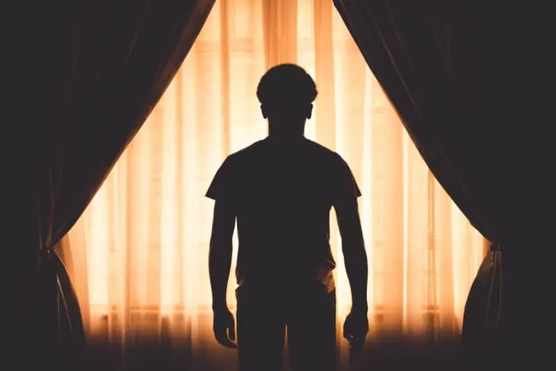 silhouette of man standing near window with curtain