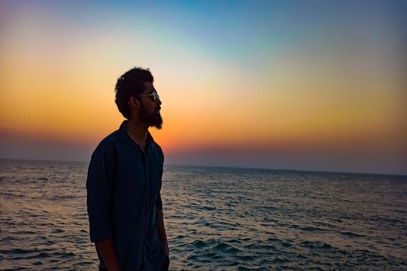 man in blue polo shirt standing on beach during sunset