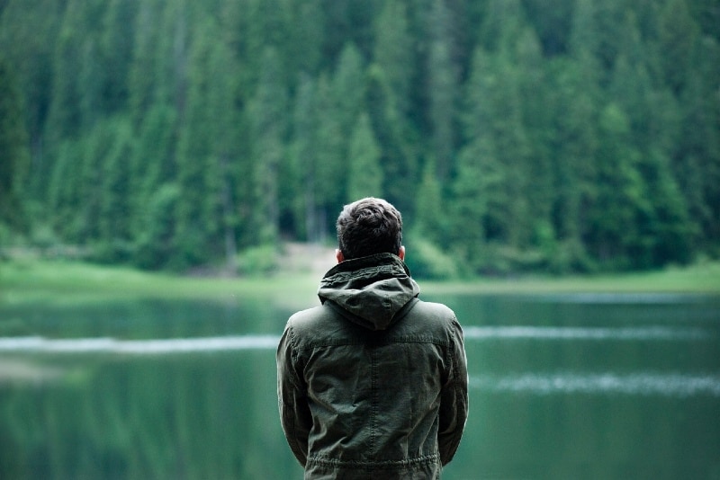 man in hooded jacket looking at water