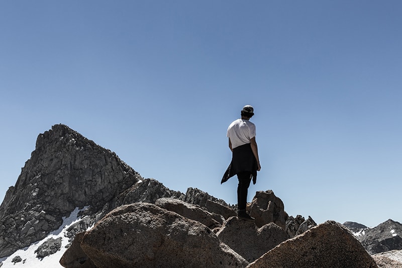 uomo in piedi su roccia picco di montagna sotto il cielo blu