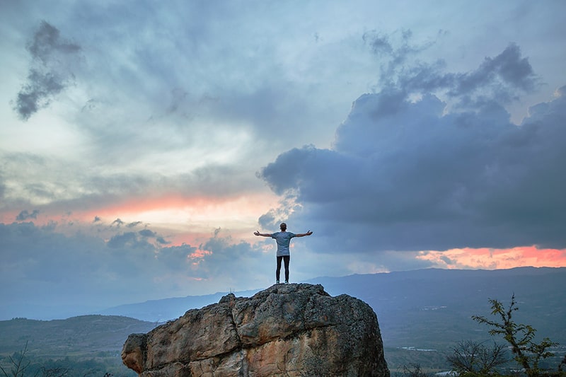 uomo in piedi sulla cima della montagna rocciosa durante l'ora d'oro