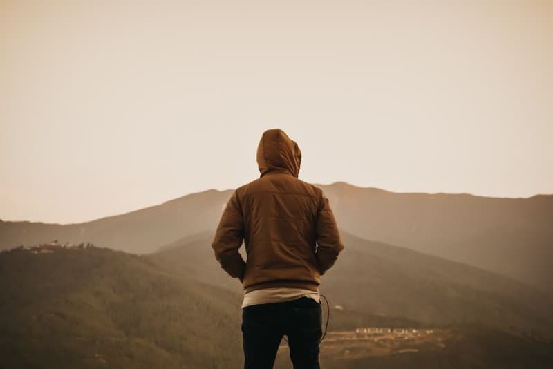 man in brown hoodie looking at mountain