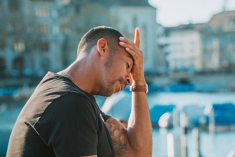 man touching his forehead with his left palm near boats