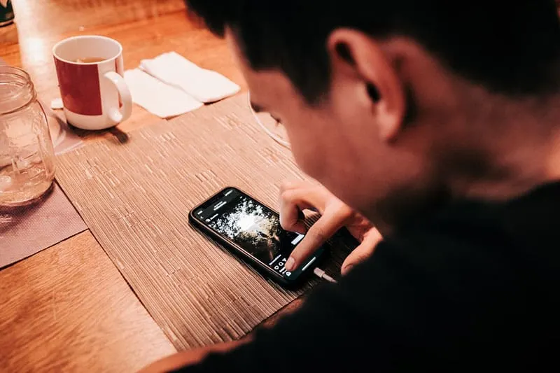man touching phone placed on a wooden table