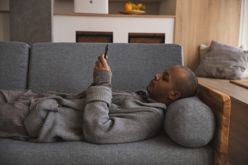 hombre utilizando su teléfono móvil tumbado en un sofá