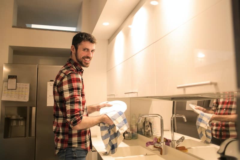 man washing plates staring while smiling with a mirror in the sink