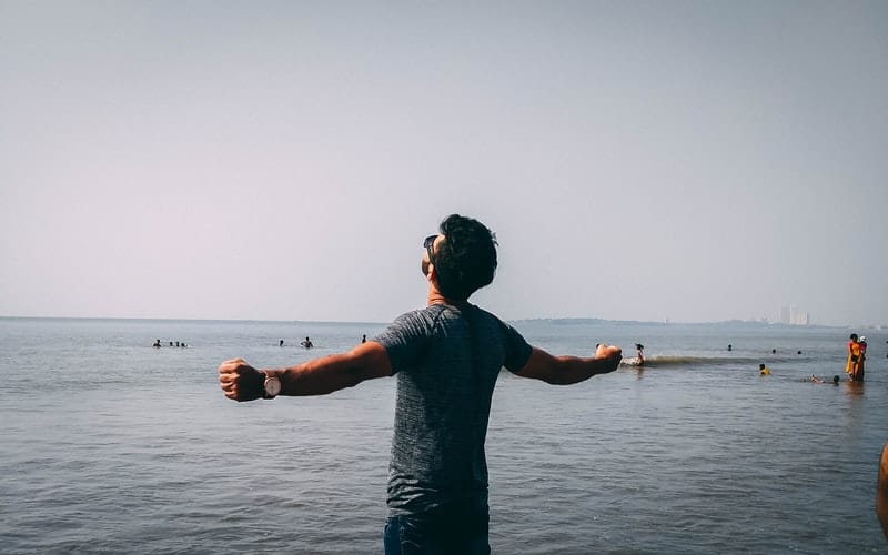 uomo in camicia grigia vicino al mare con le braccia alzate