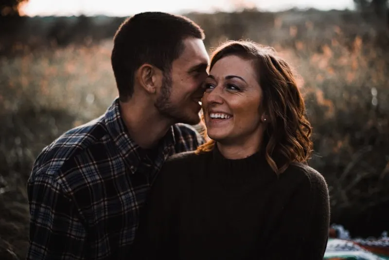 man whispering in woman's ear while standing outdoor