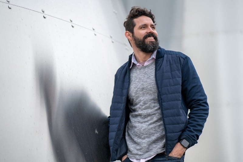 man in blue zip up jacket standing beside white wall