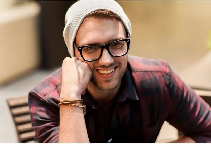 man with fist on his face smiling wearing a bonnet, eyeglass and checkered top