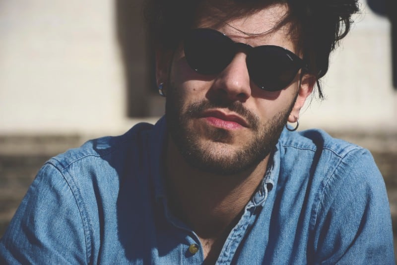 hombre con camisa vaquera y gafas de sol negras sentado al aire libre