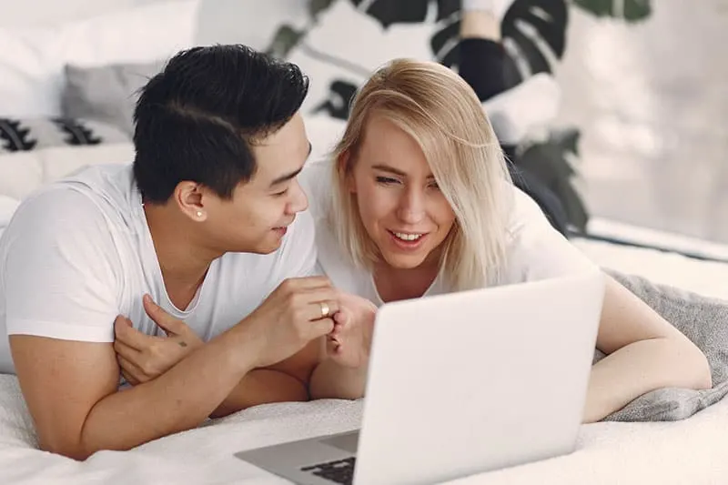 man and woman using macbook while on bed 
