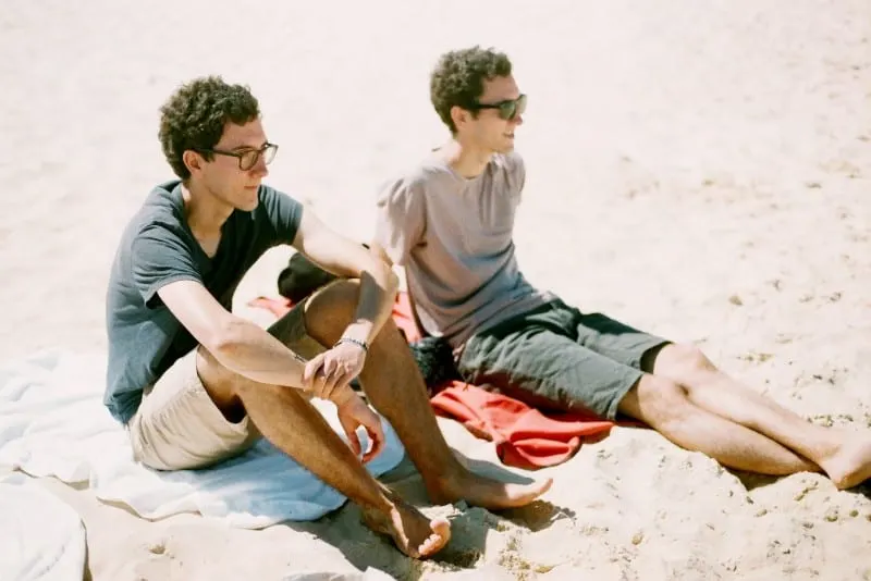 twin males sitting on beach 