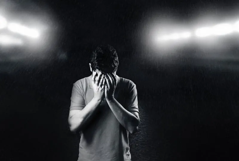 monochromatic photo of man covering his face with 2 lights in the background