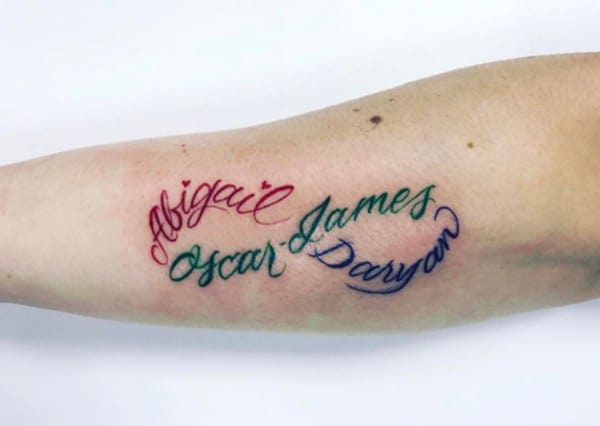 colorful names in cursive tattoo on arm