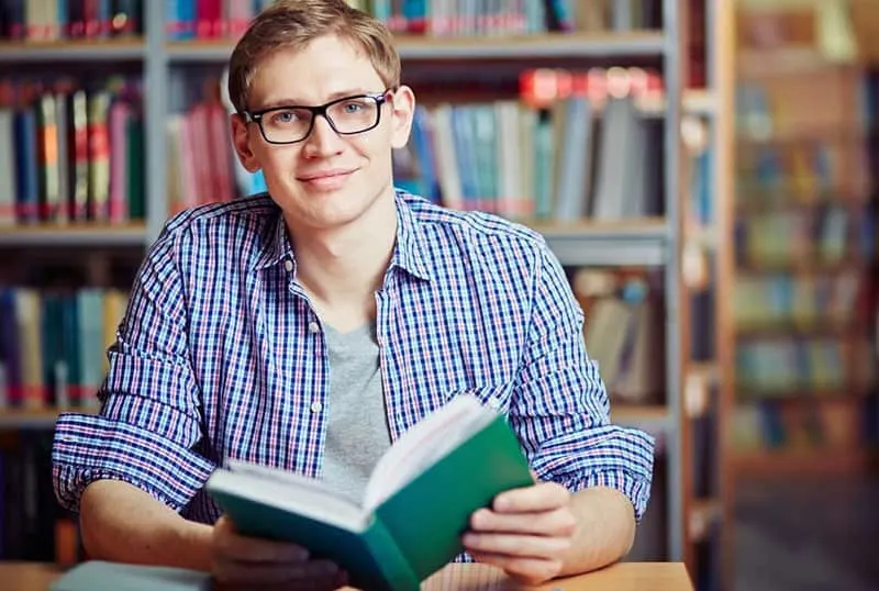 nerd guy holding a book inside a library
