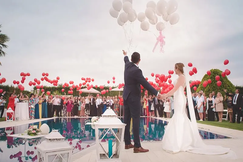 newlyweds standing in front of guests while holding a balloons