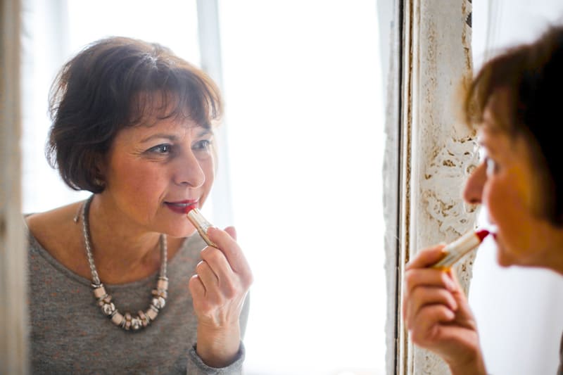 older woman applying lipstick in front of the mirror