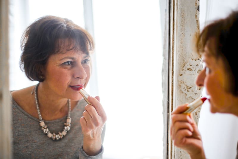 mujer mayor pintándose los labios frente al espejo