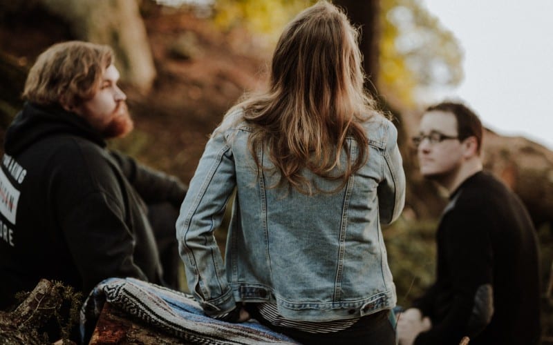 One woman sitting between two man on the ground in the forest