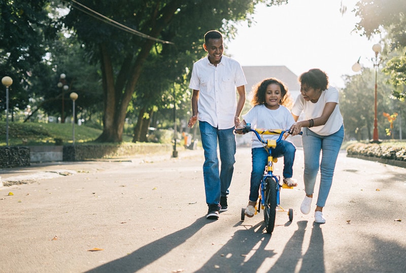 parents teaching their child how to ride a bike on empty street