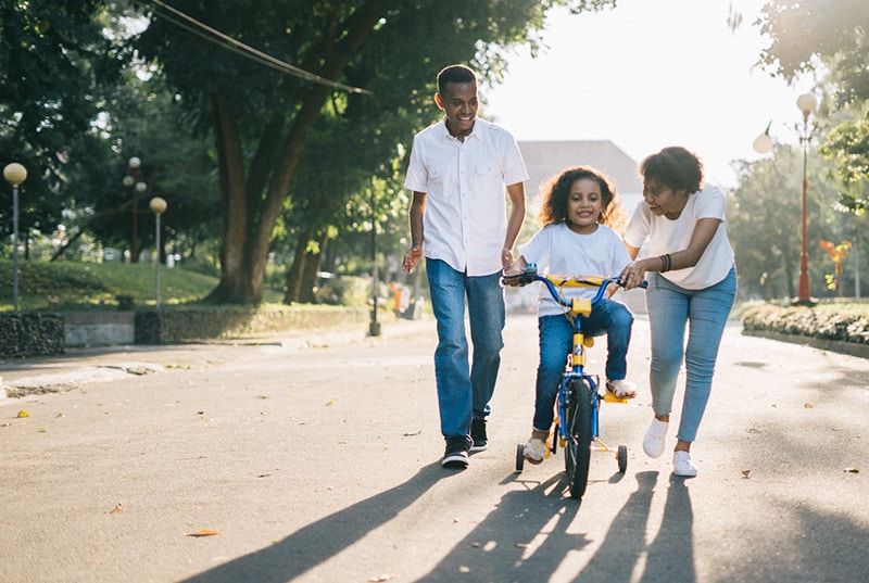 pais que ensinam o filho a andar de bicicleta numa rua vazia