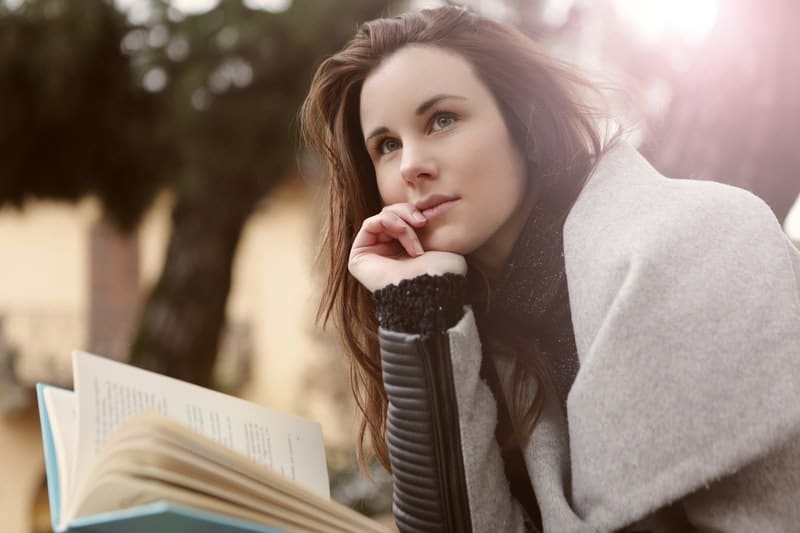 mujer pensativa con abrigo gris sosteniendo un libro