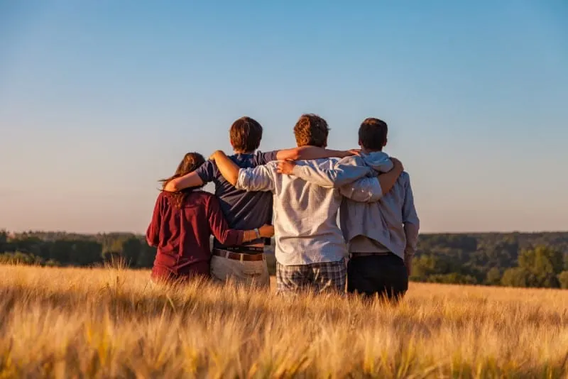 four people standing and hugging in the field