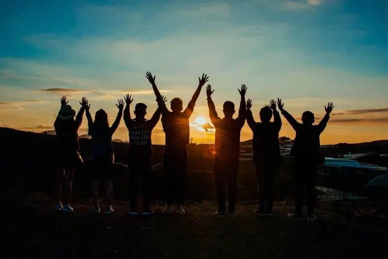 seven people put hands up during sunset